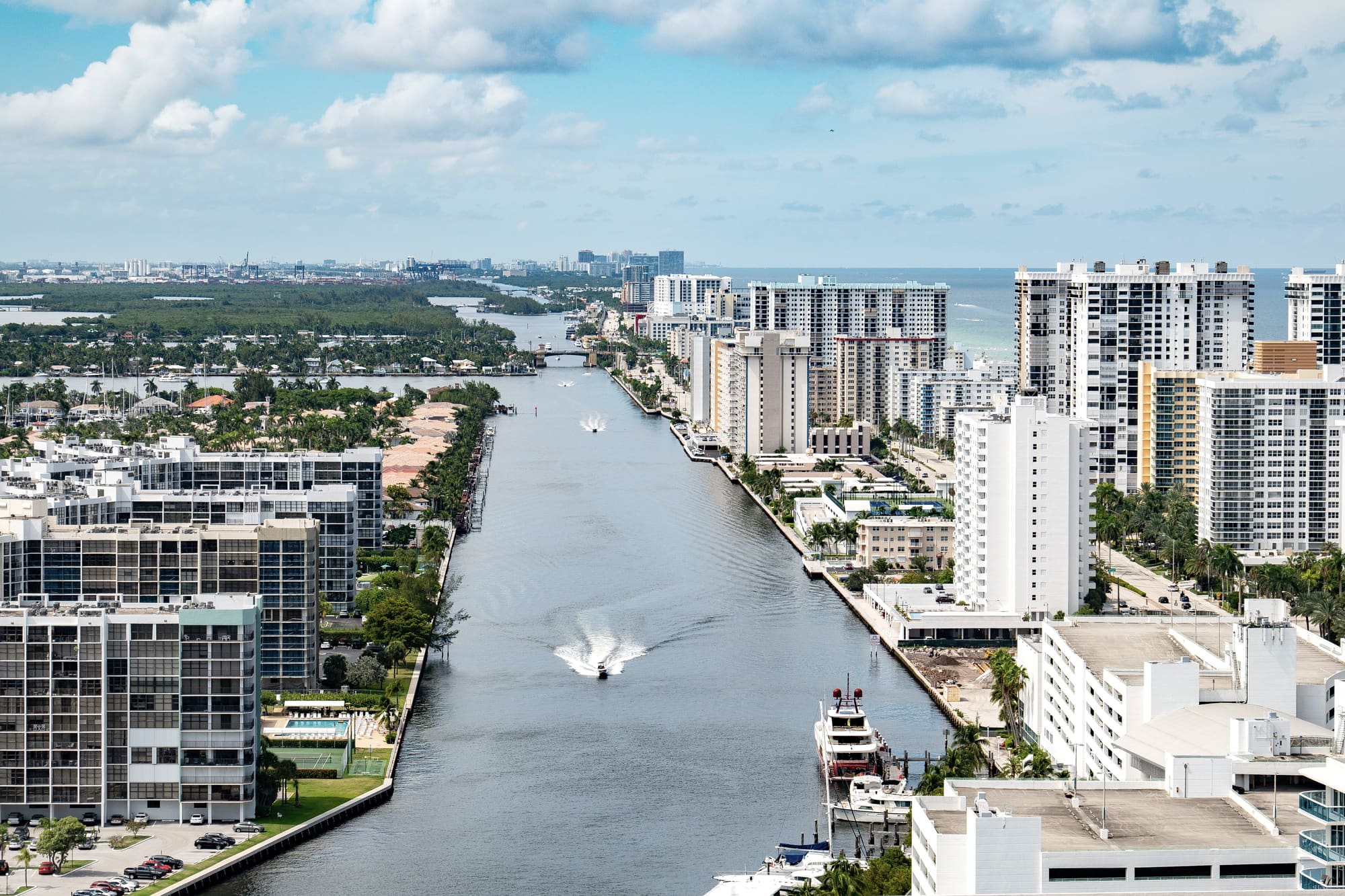 Aerial view along a South Florida waterway lined with mid-rise and high-rise residential buildings, the ocean beyond them
