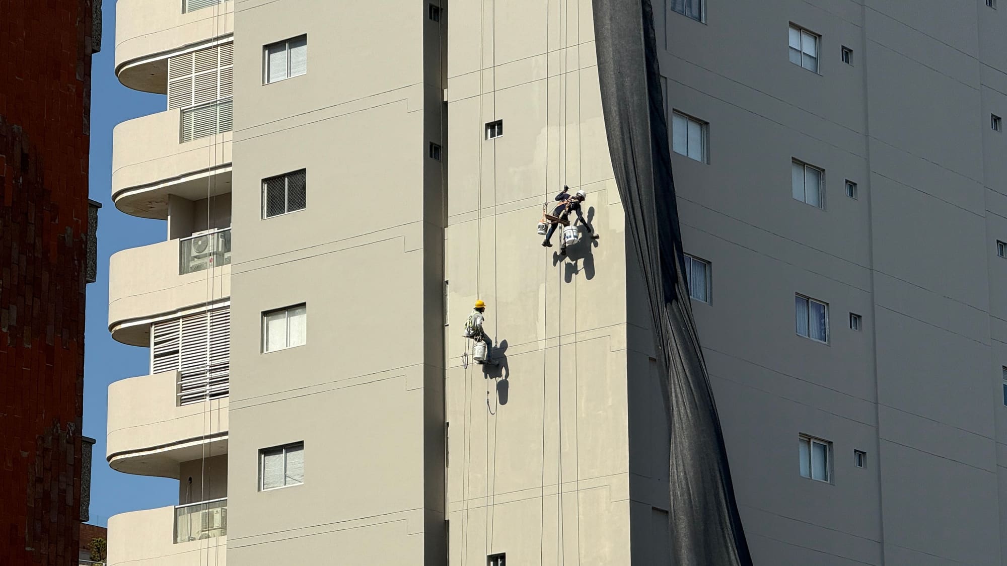 Técnicos en cuerda inspeccionando la fachada con balcones de una torre de concreto