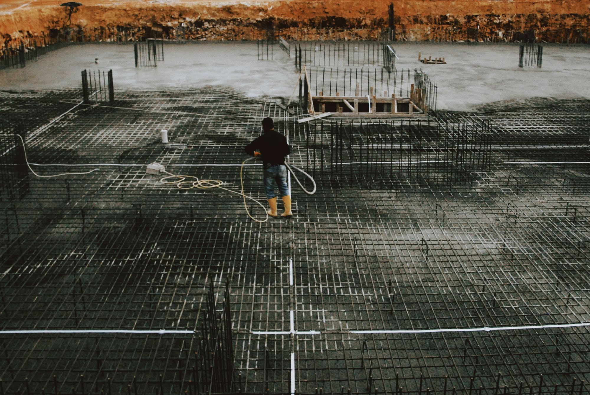 Mat foundation reinforcement laid out inside an excavation, a worker checking the bars