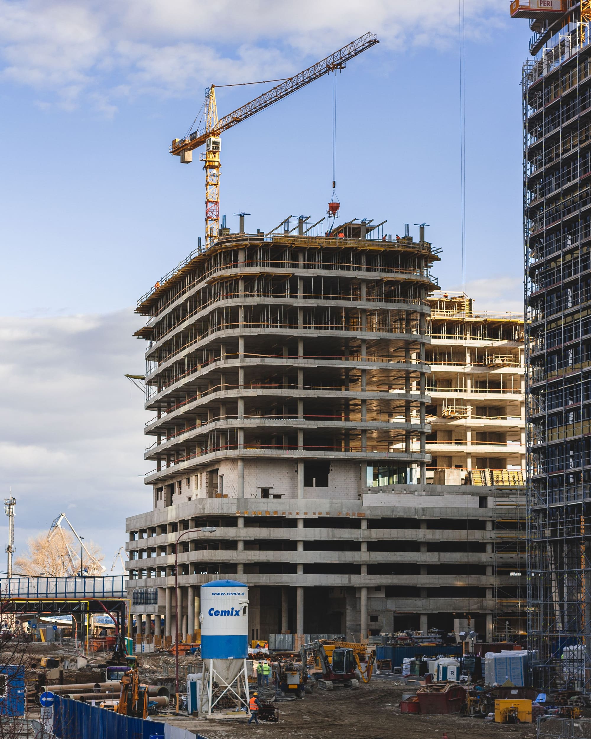 Multi-storey reinforced-concrete frame under a tower crane, floor plates open to the sky