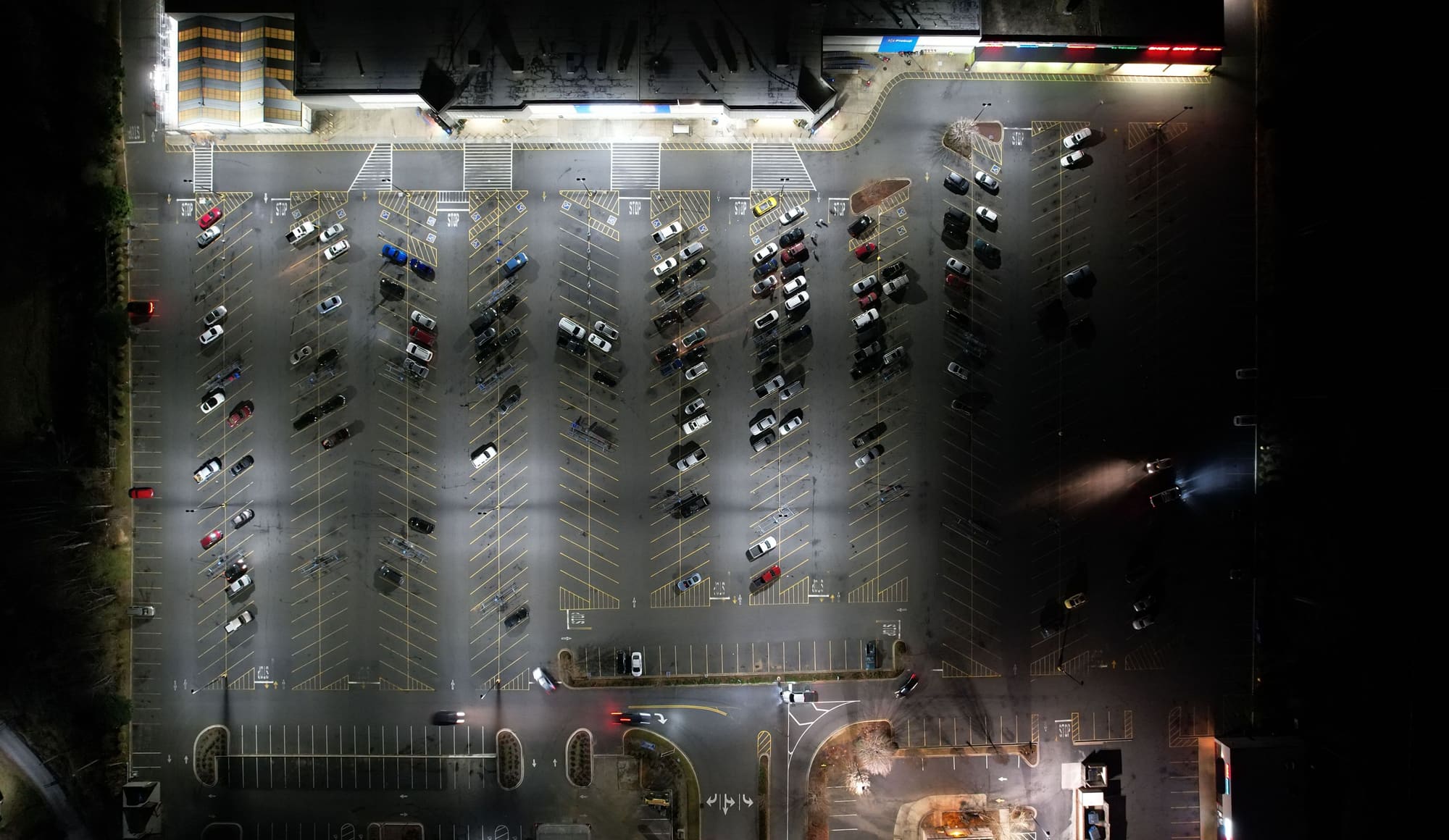 Un estacionamiento de noche visto desde arriba, iluminado por sus postes