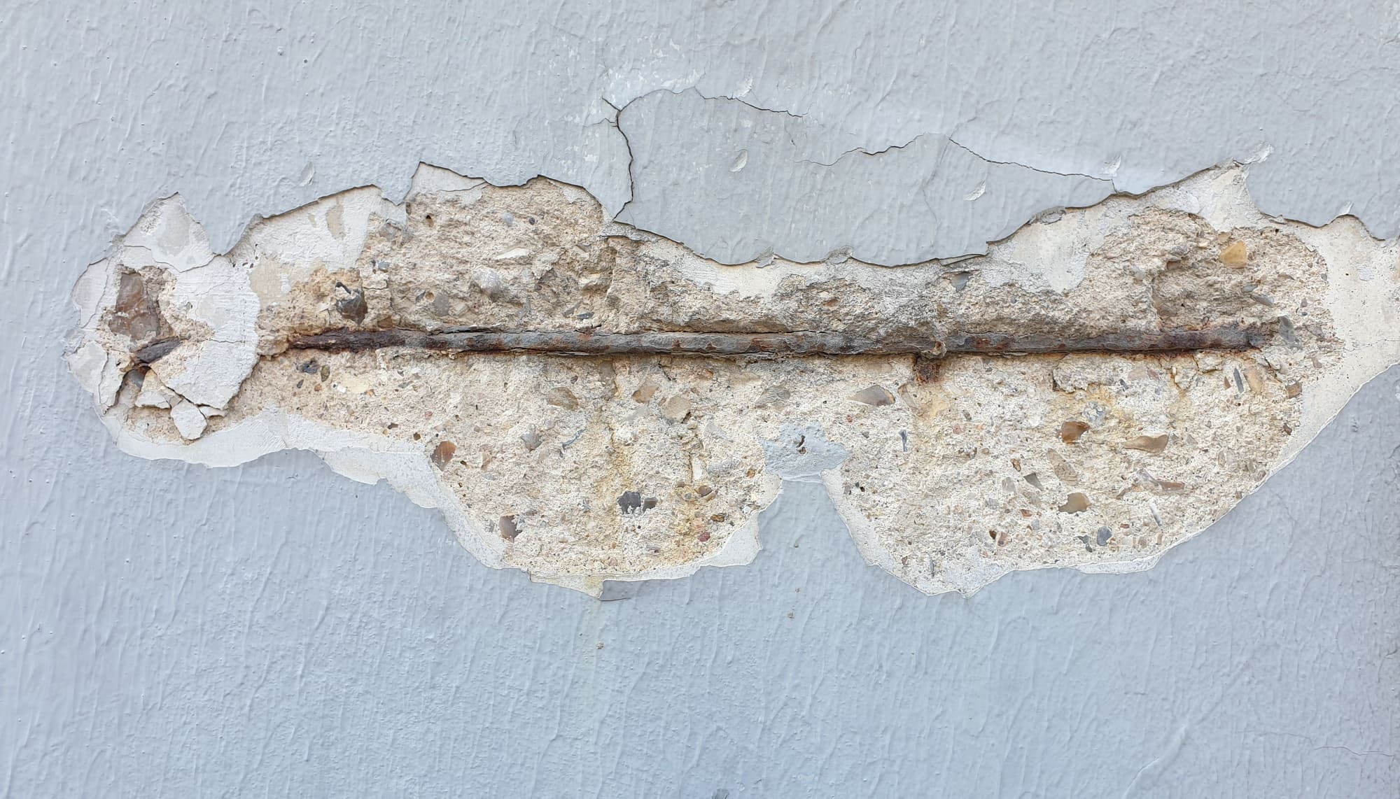 Concreto desprendido en un muro pintado, con la varilla oxidada a la vista
