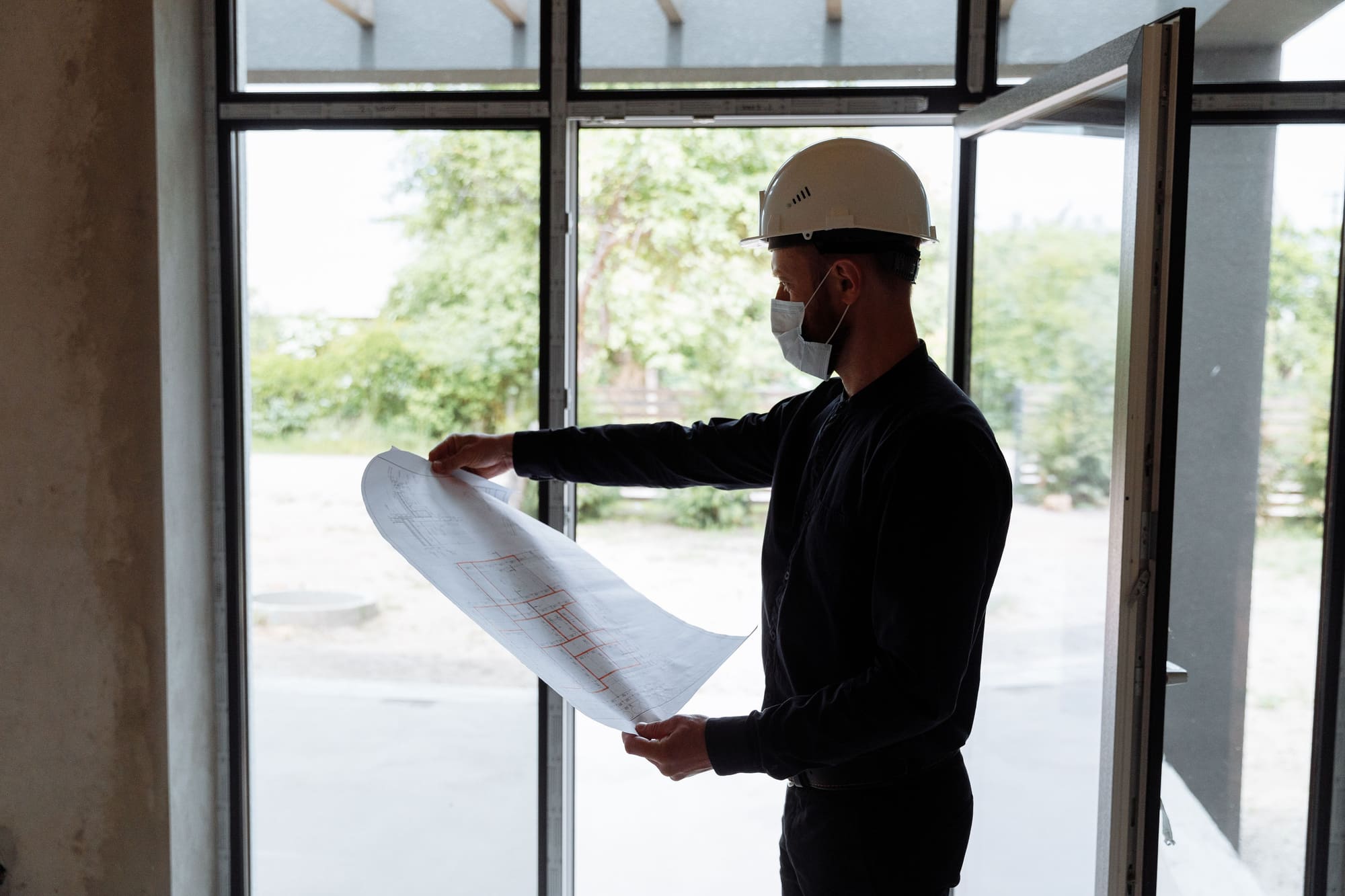 Inspector in a hard hat reading the drawings at the window of a building under inspection