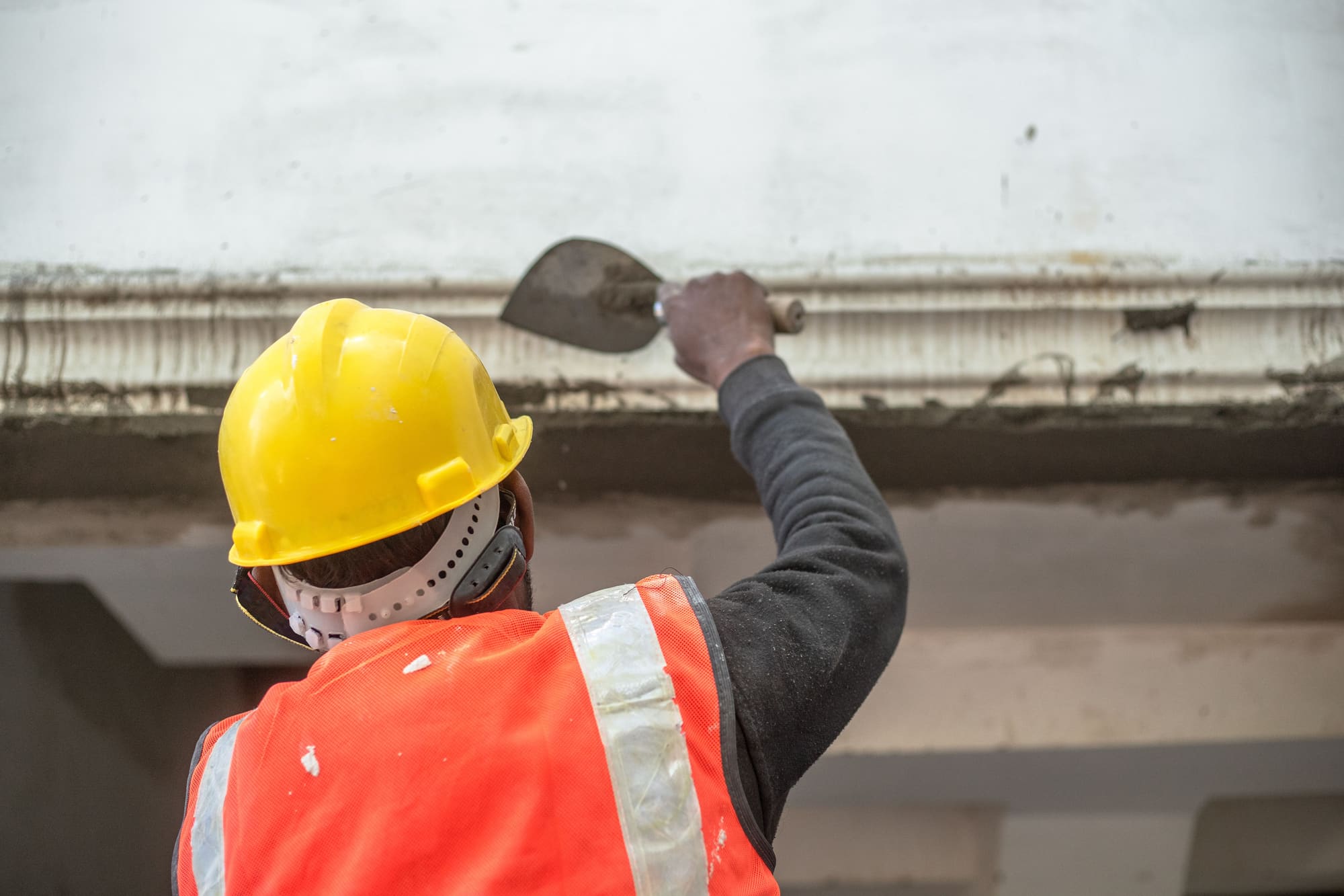 Worker in a hard hat patching the underside of a concrete beam with a trowel