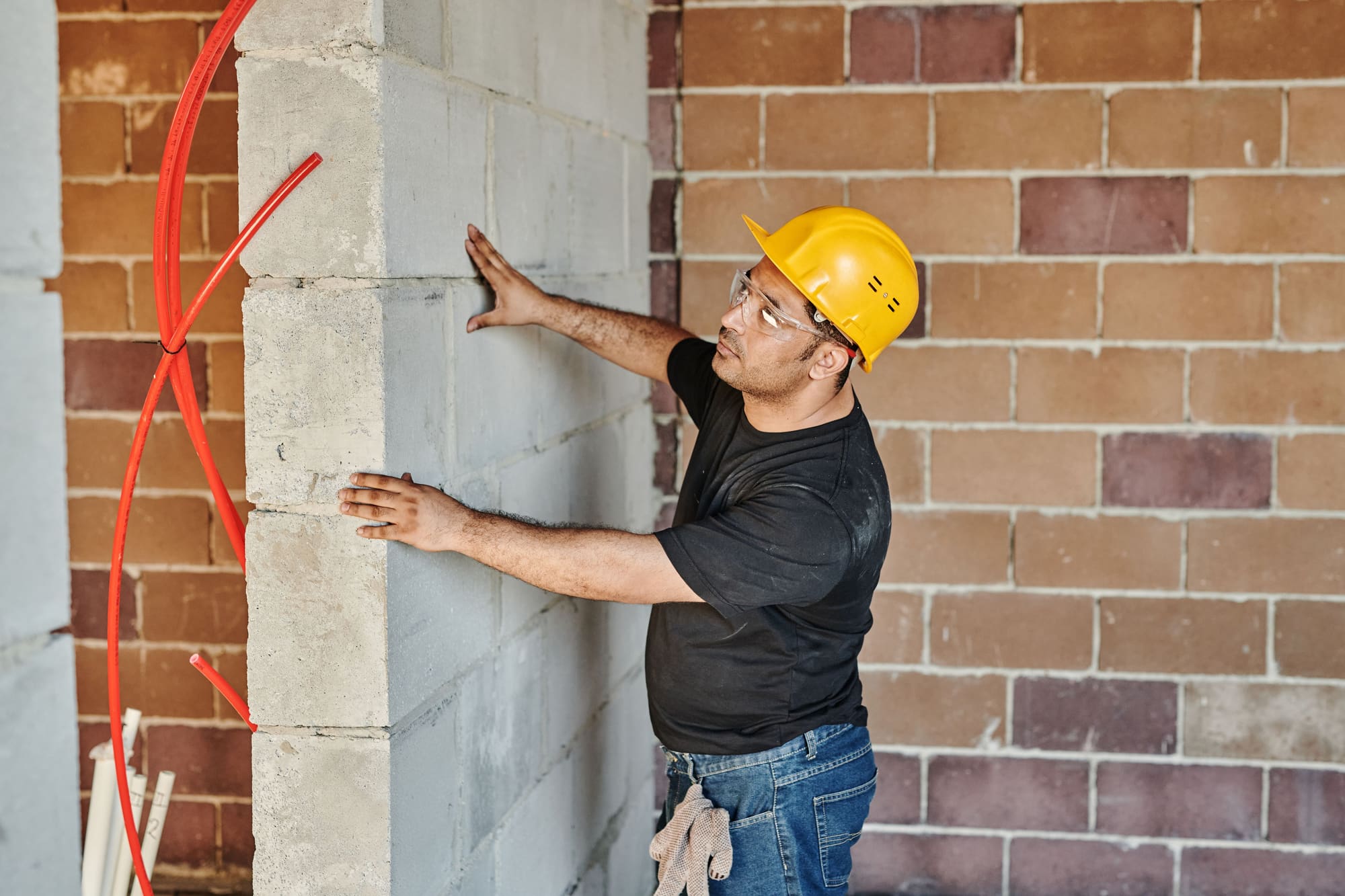 Un inspector con casco revisa a mano un muro de bloques