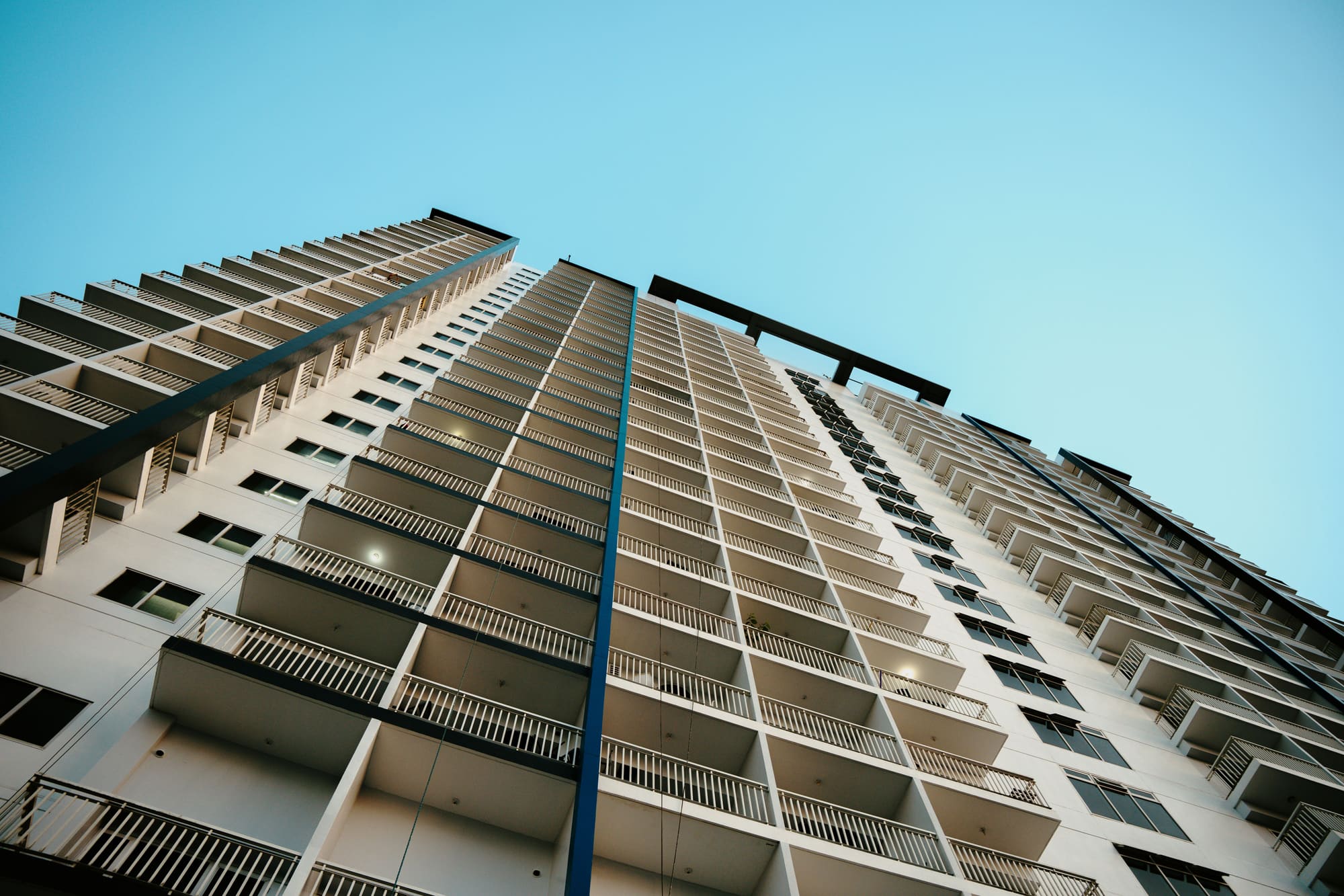 Tall condominium tower of stacked balconies against a clear sky, seen from the street